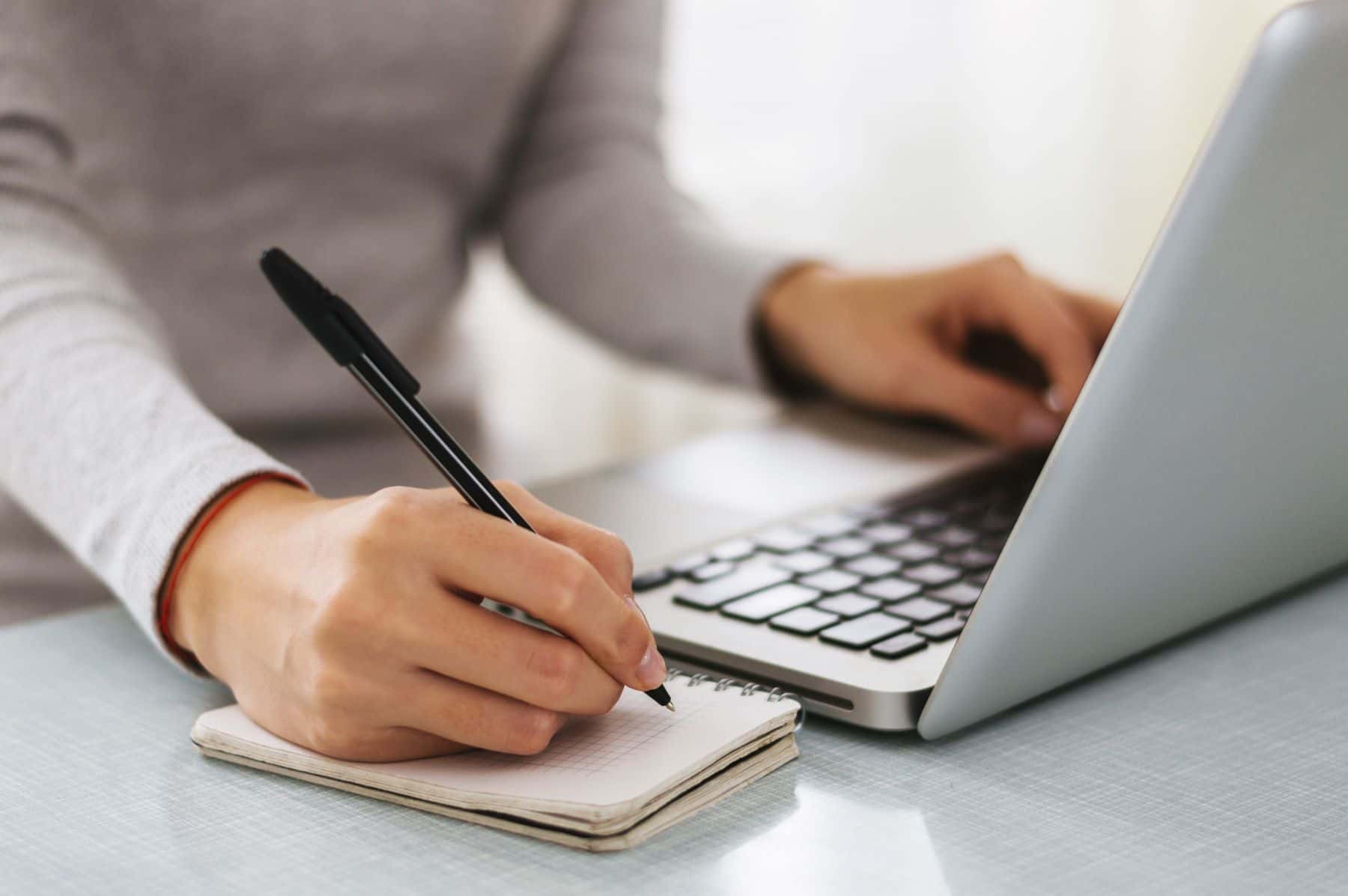 Person writing while using laptop computer