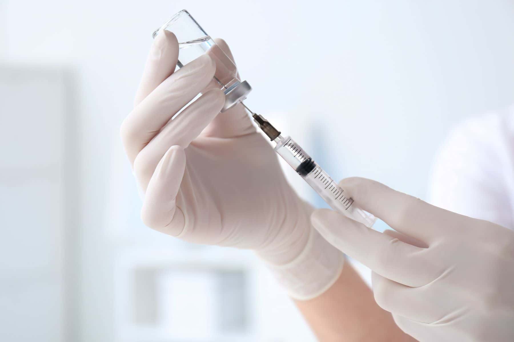 Doctor filling syringe with medication from vial