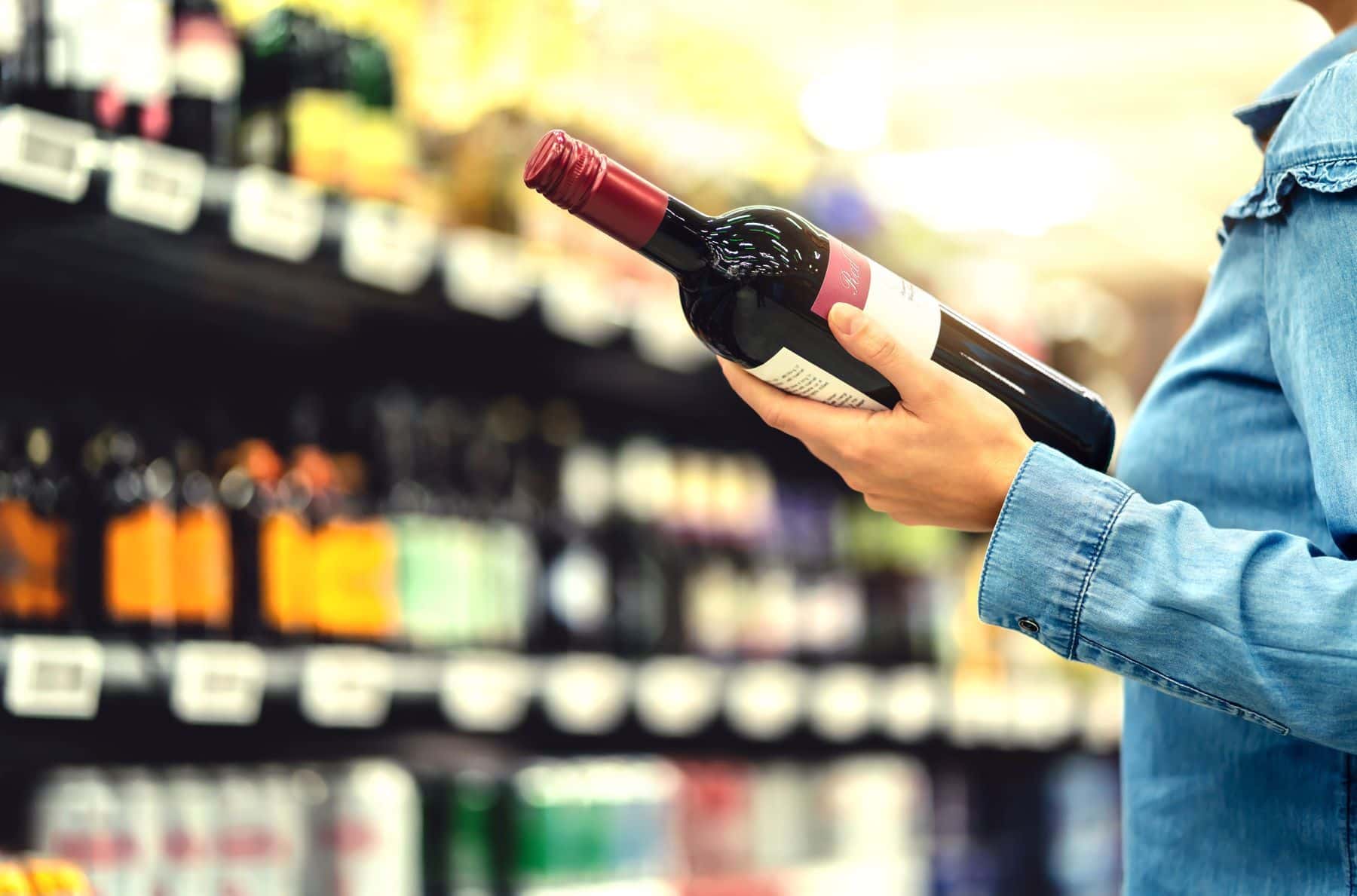 Person buying a bottle of red wine in a dram shop