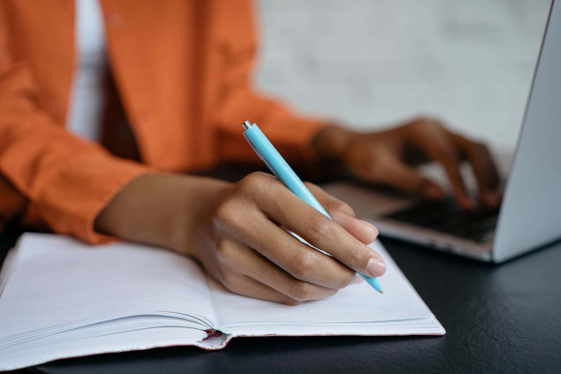 Person writing while using a laptop