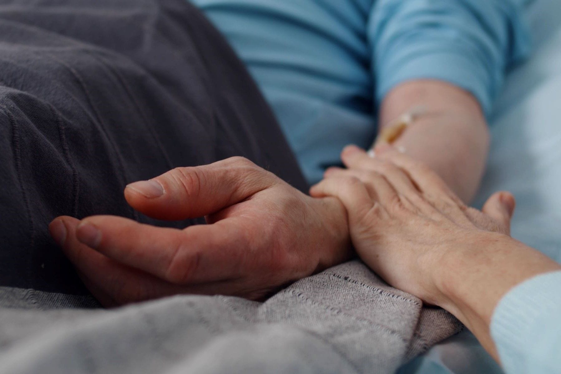 Close up of aged woman sitting by bed of sick husband and holding hands
